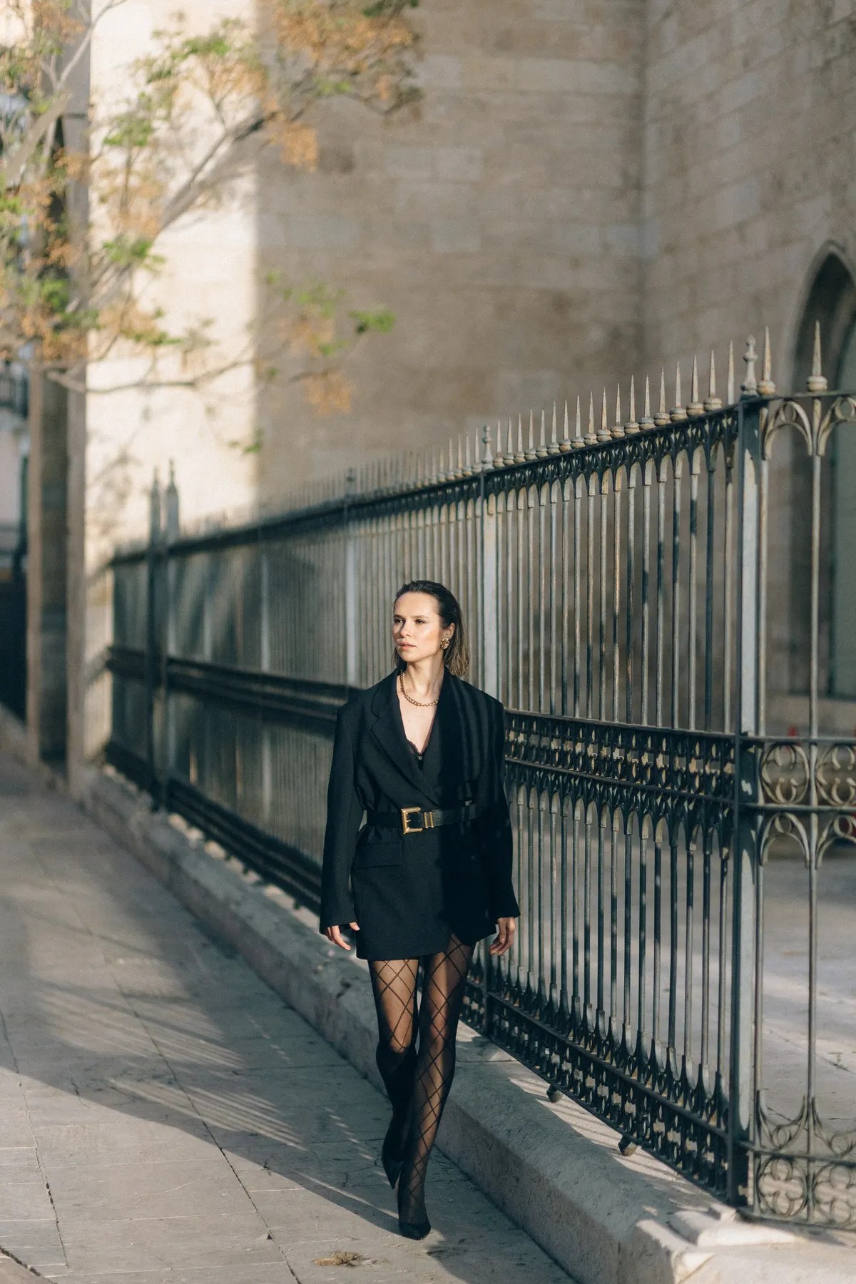 Woman in a black belted blazer dress walking on a city street