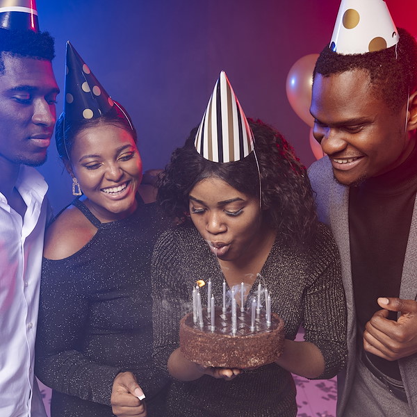 Friends in party hats gathered around a birthday cake as the candles are blown out