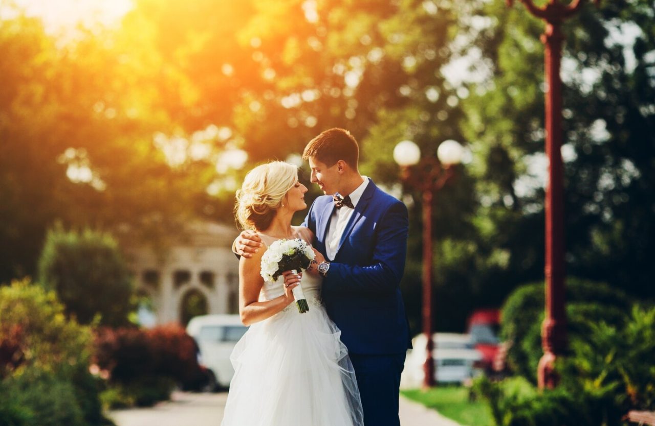 Bride holding a white bouquet embracing the groom in golden evening light