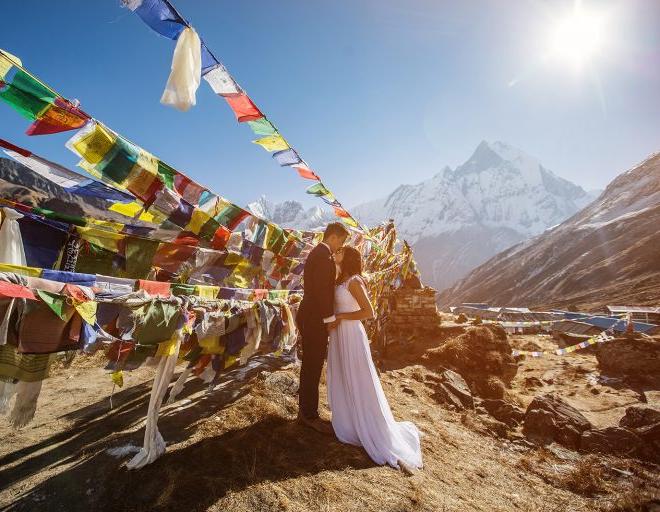 Bride and groom kissing beside colourful prayer flags on a mountain trail