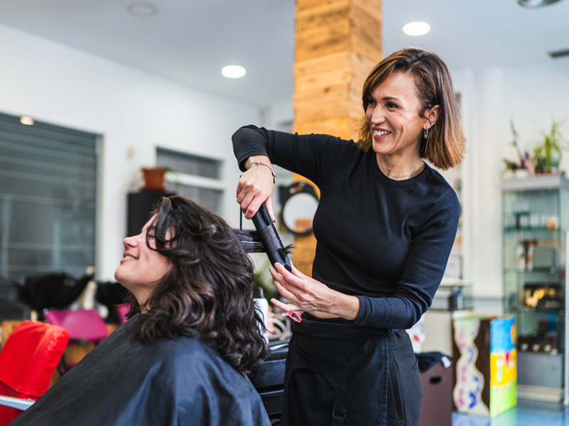 Stylist straightening a client's dark wavy hair with a flat iron