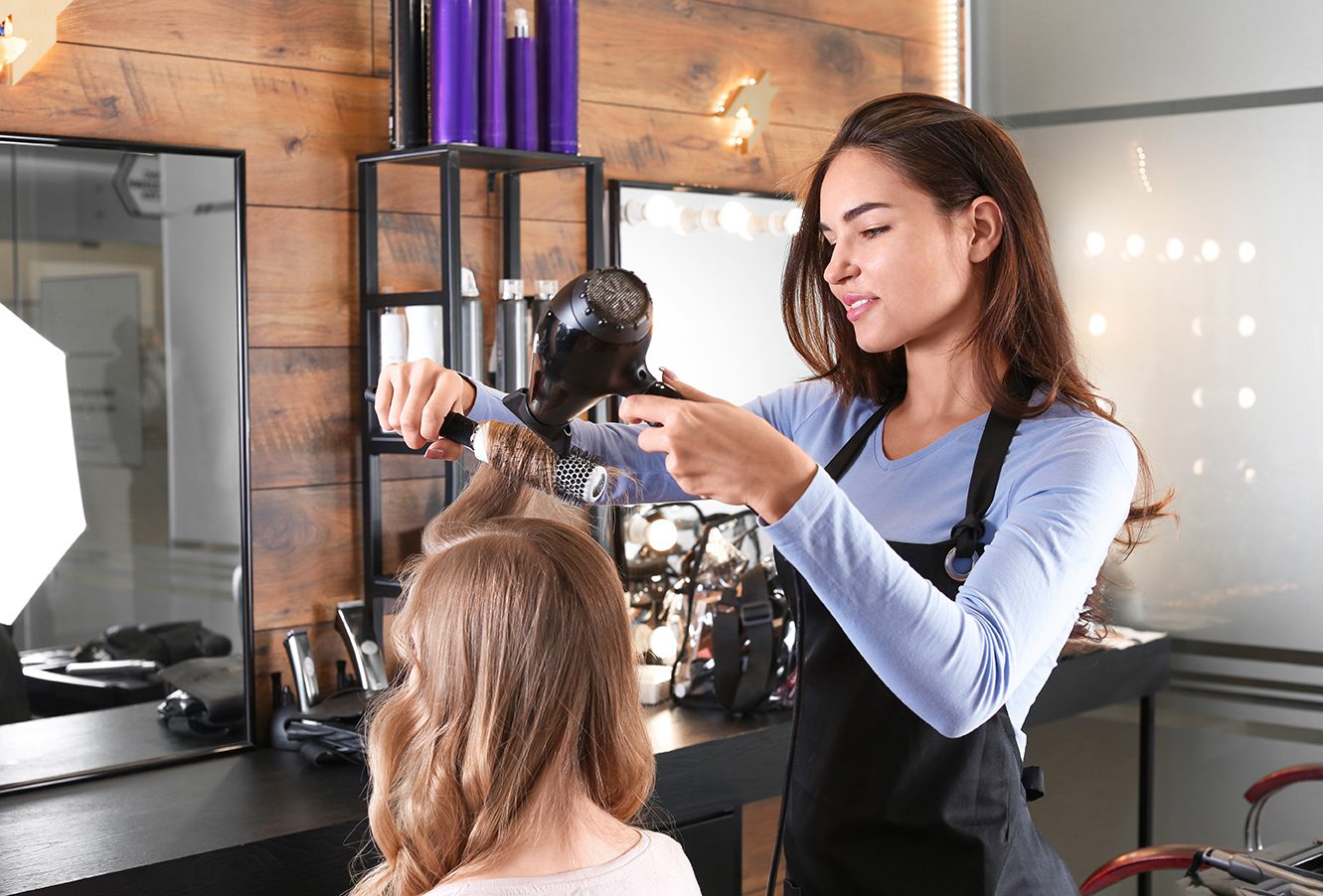 Stylist blow-drying a client's blonde hair with a round brush